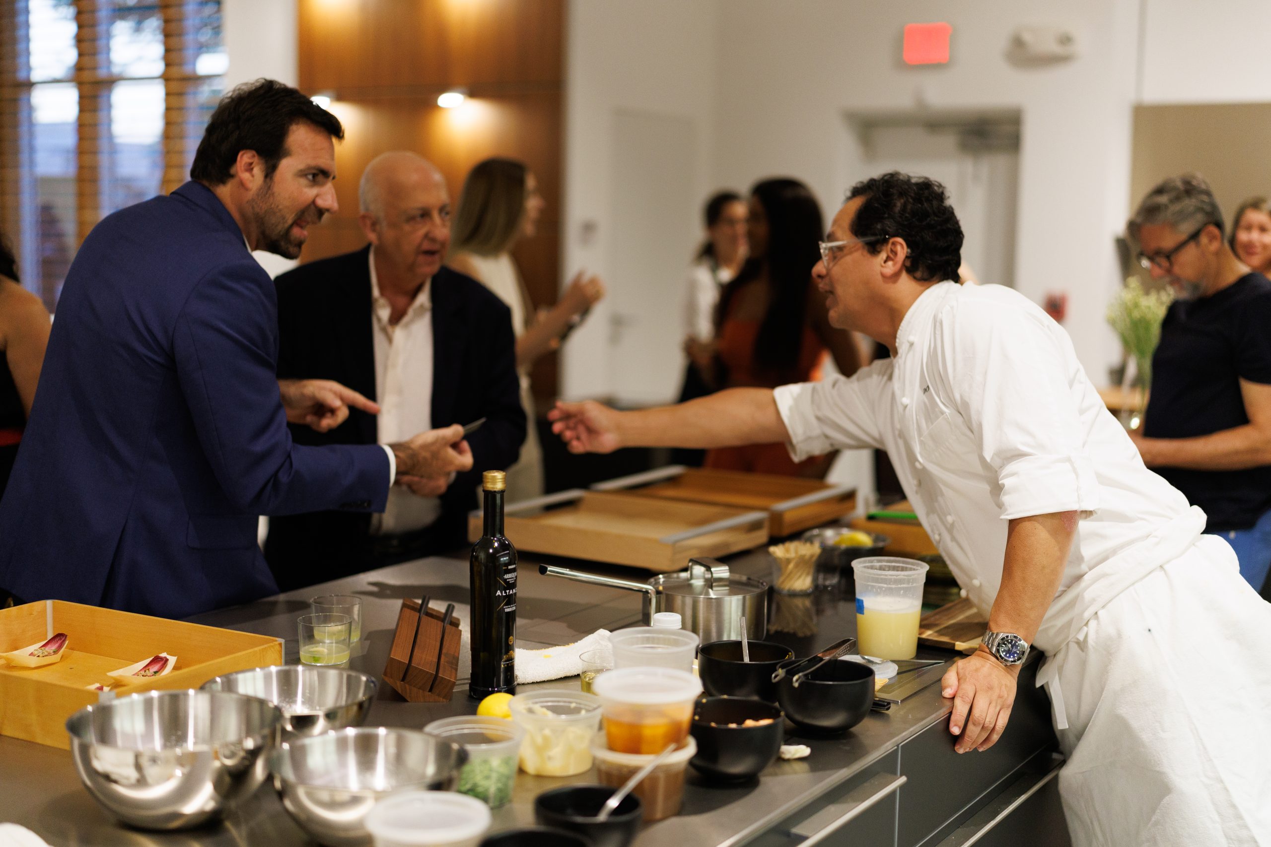 bulthaup Miami showroom and bulthaup b3 kitchens featuring minimalist cabinetry and stainless steel bulthaup countertop with event guests and chef enjoying conversation.